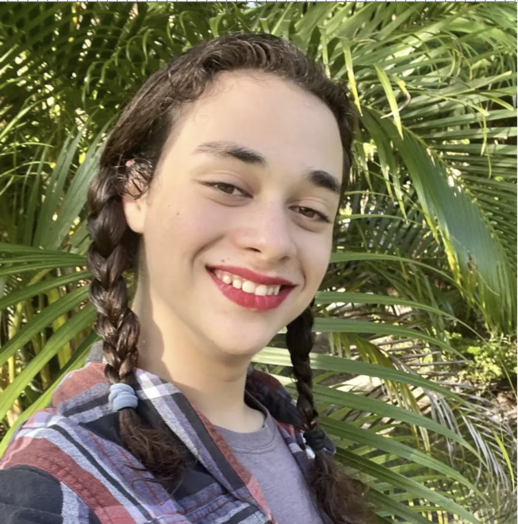 Emily Keller poses for a selfie in front of a leafy plant. 